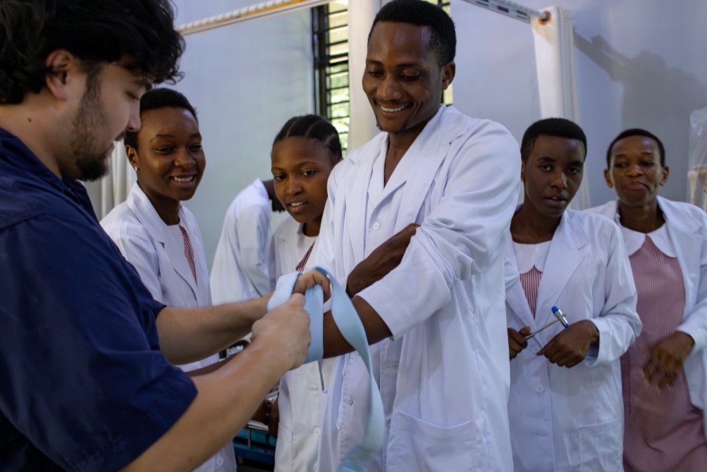 Healthcare students in lab coats learning a clinical procedure with an instructor