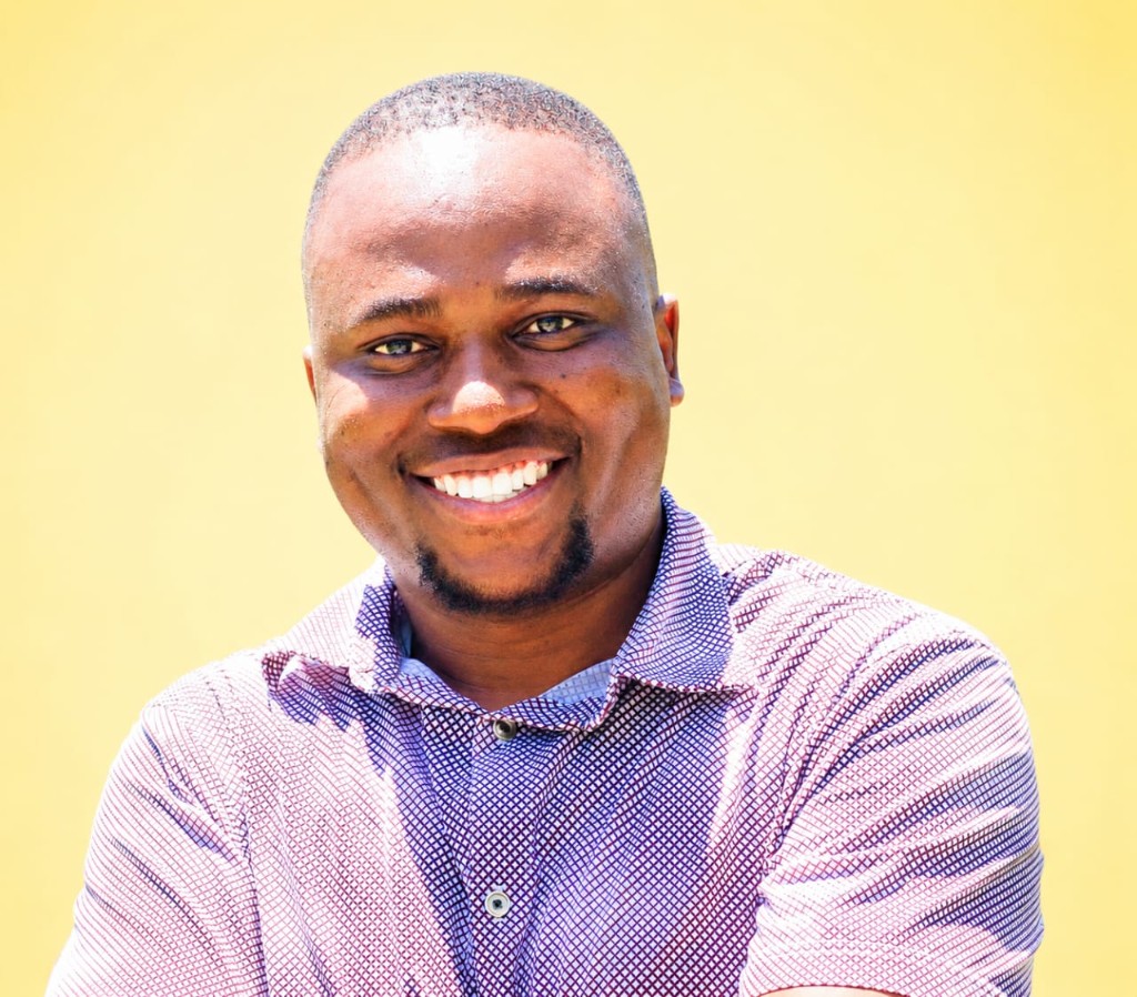 Professional portrait of Julius Mageka Nalimi against a yellow background